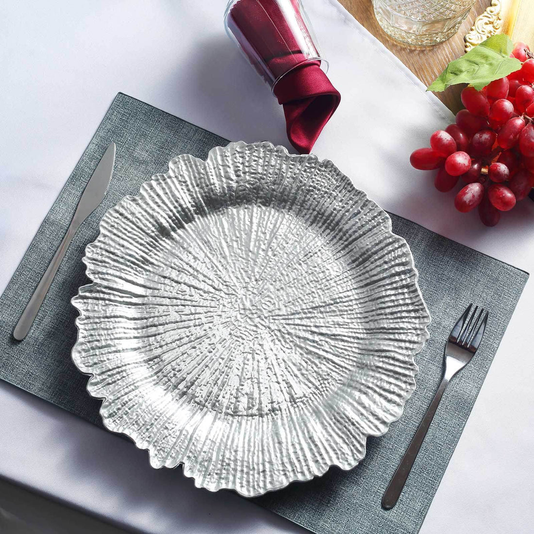 Decorative silver plate on a textured placemat with cutlery and grapes.
