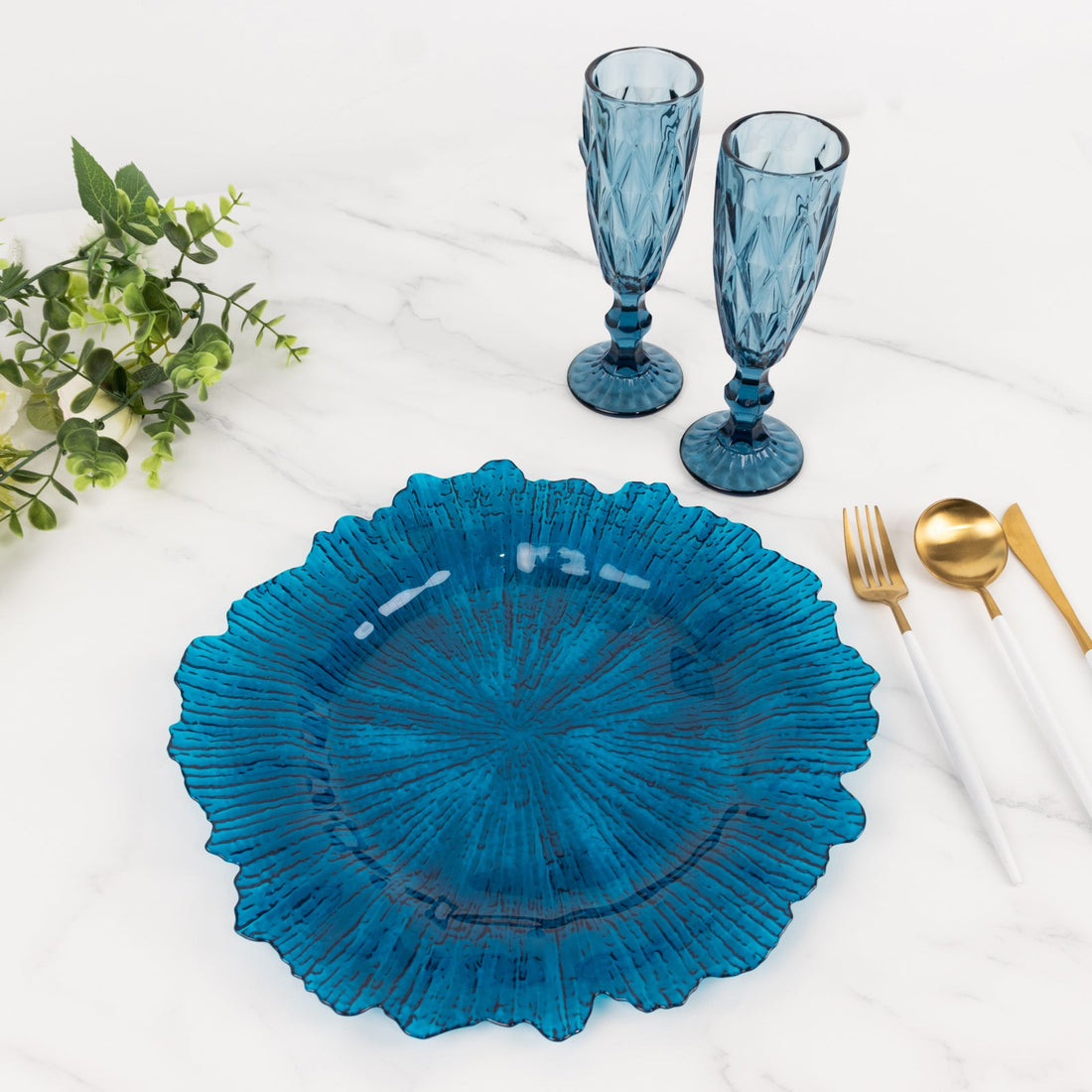 Blue decorative plate with two textured glasses and gold utensils on a marble surface.