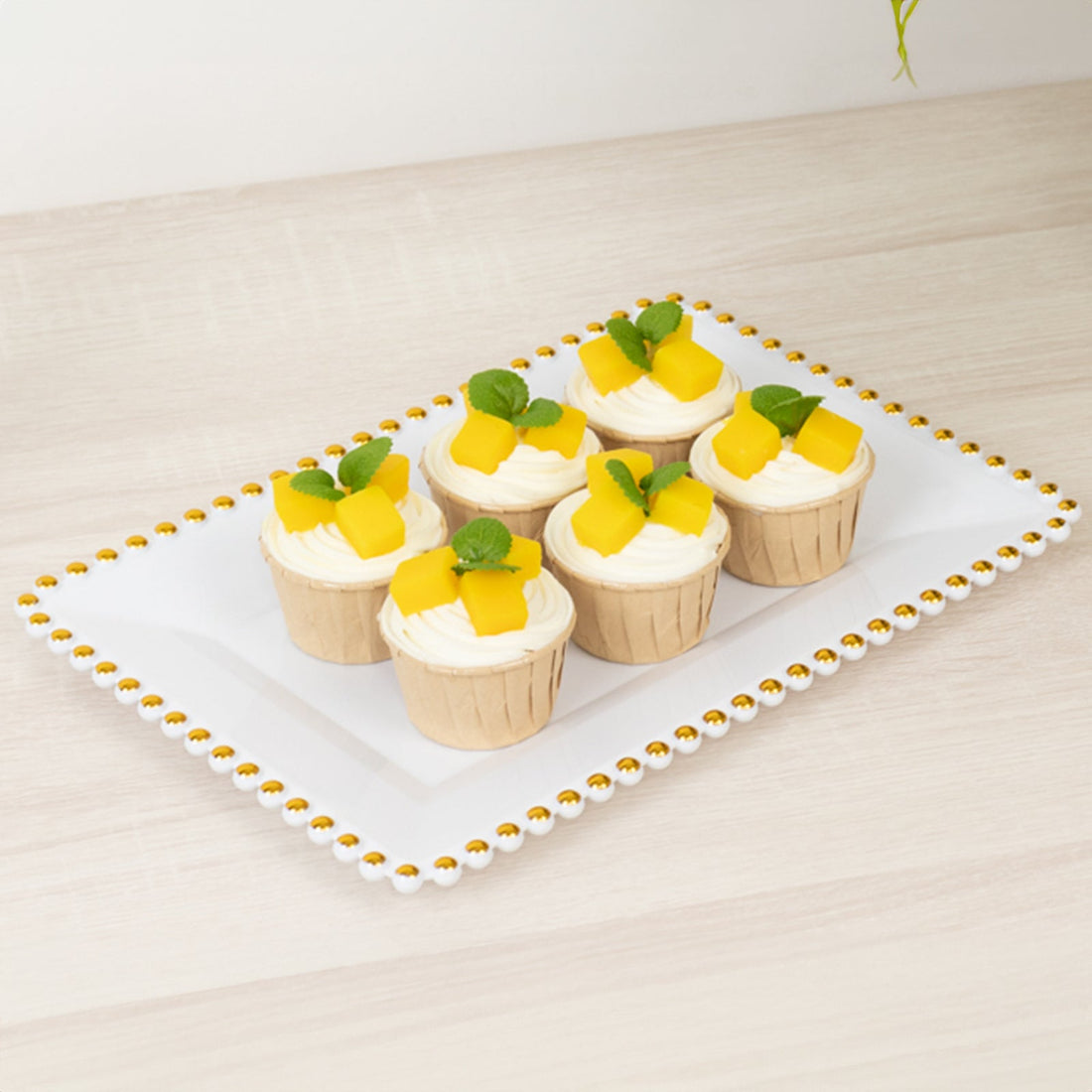 Cupcakes with mango topping and mint leaves on a decorative platter.