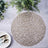 Round woven placemat in natural tones on a textured surface.