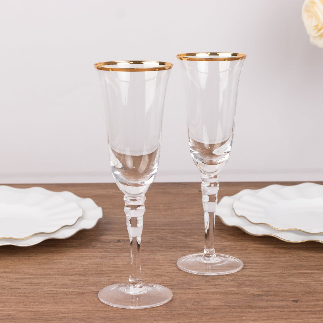 Elegant crystal champagne flutes with gold rim on a wooden table.