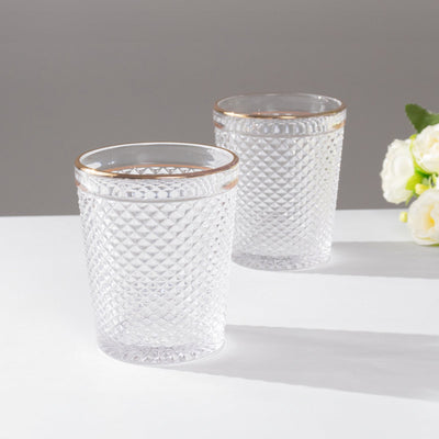 Set of two crystal glasses with gold rim on a plain background.