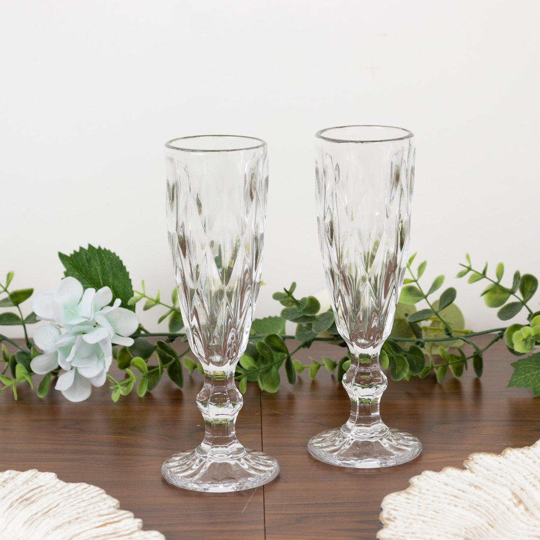 Crystal champagne flutes on a wooden table with greenery.