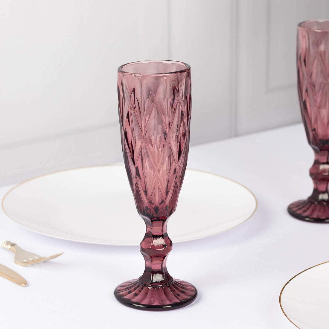 Purple crystal champagne flute on a white table with elegant dining setup.
