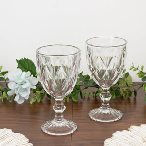 Set of two elegant crystal goblets on a wooden table with greenery.