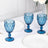 Set of three blue glass goblets on a table with white plates and floral decor.