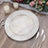 Elegant round plate with textured design on wooden table, surrounded by candles and flowers.