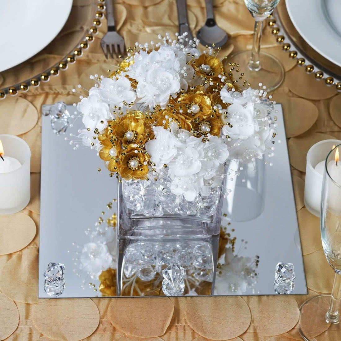 Elegant gold and white floral centerpiece on a mirrored table setting.