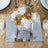 Elegant gold and white floral centerpiece on a mirrored table setting.