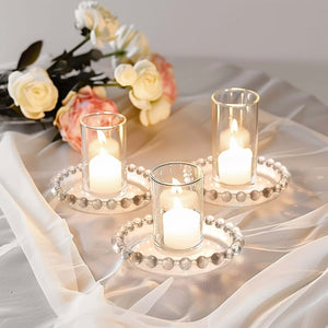 Elegant glass candle holders with candles and floral decor on a soft fabric background.