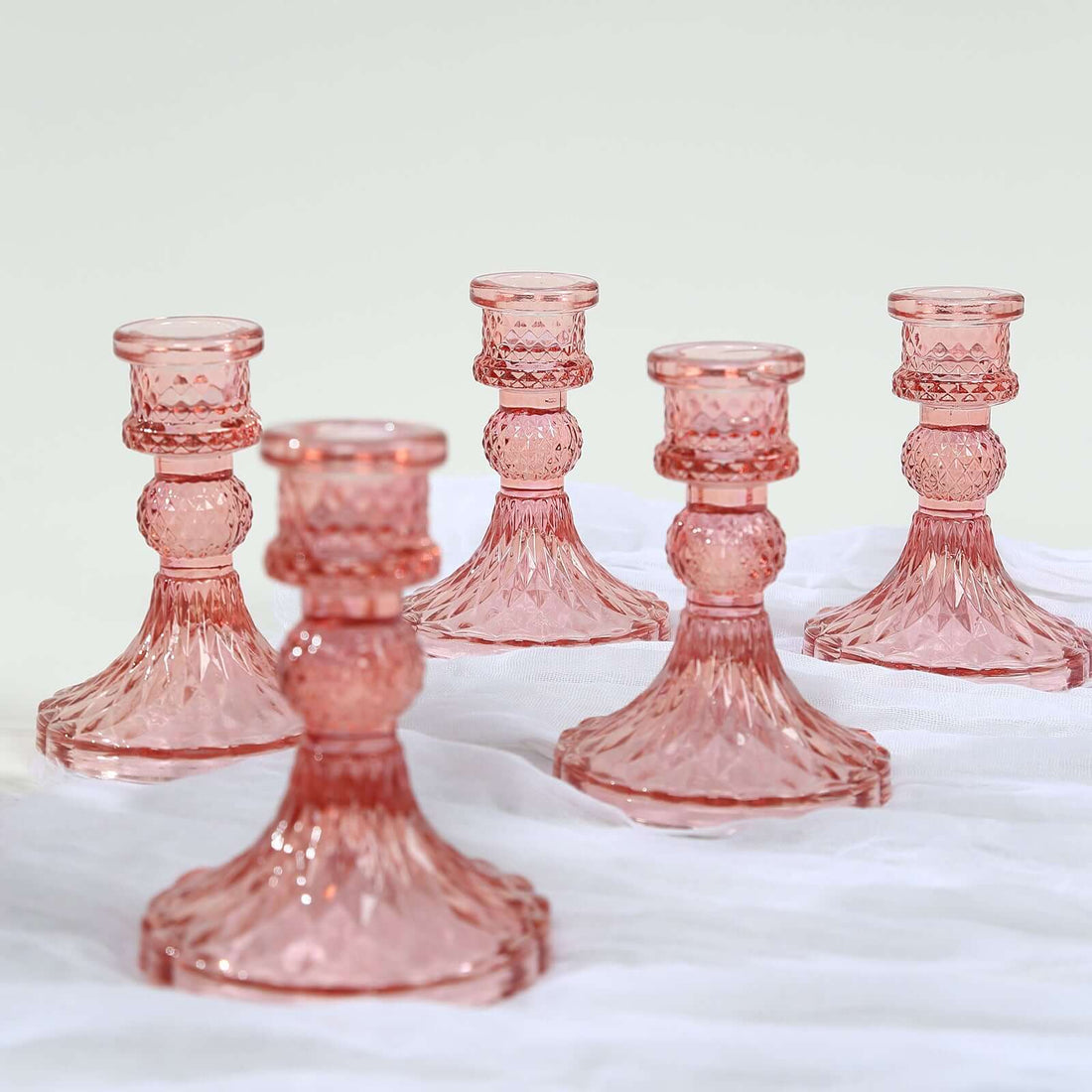 Set of five elegant pink glass candlesticks on a soft white background.
