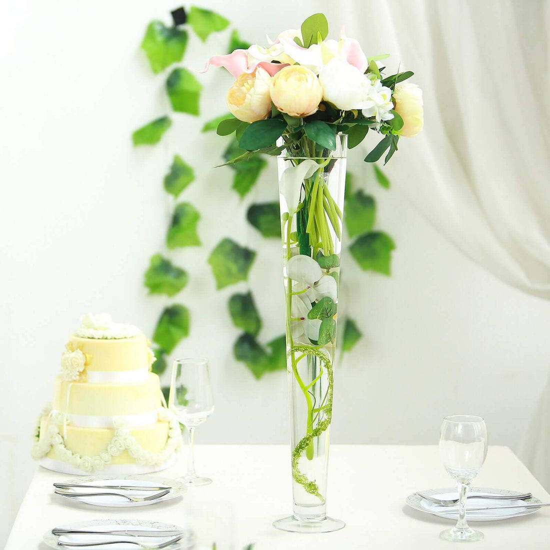 Elegant floral arrangement in a tall vase on a table with a wedding cake.