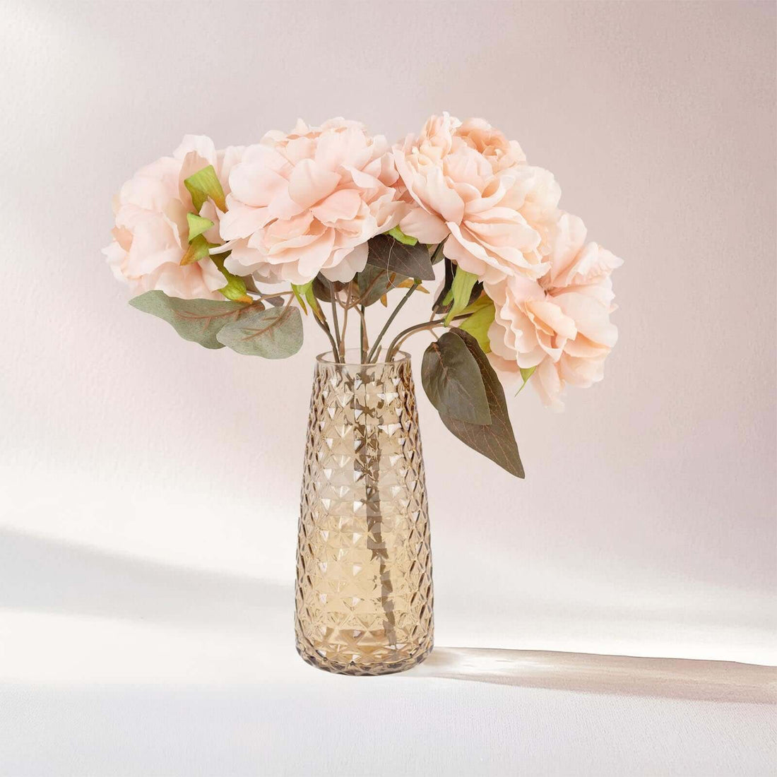 Pink peony flowers in a textured glass vase.