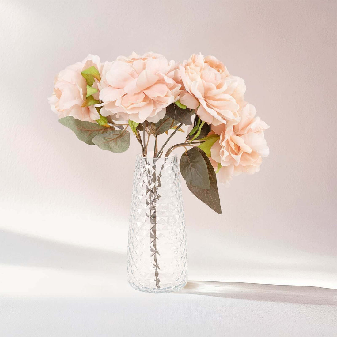 Pink faux flowers in a clear vase against a soft background.