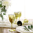 Gold wine glasses set on a table with white plates and flowers.