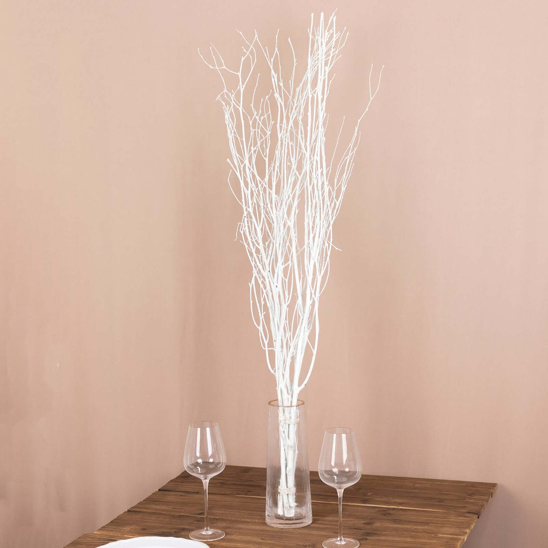 White decorative branches in a glass vase on a wooden table.