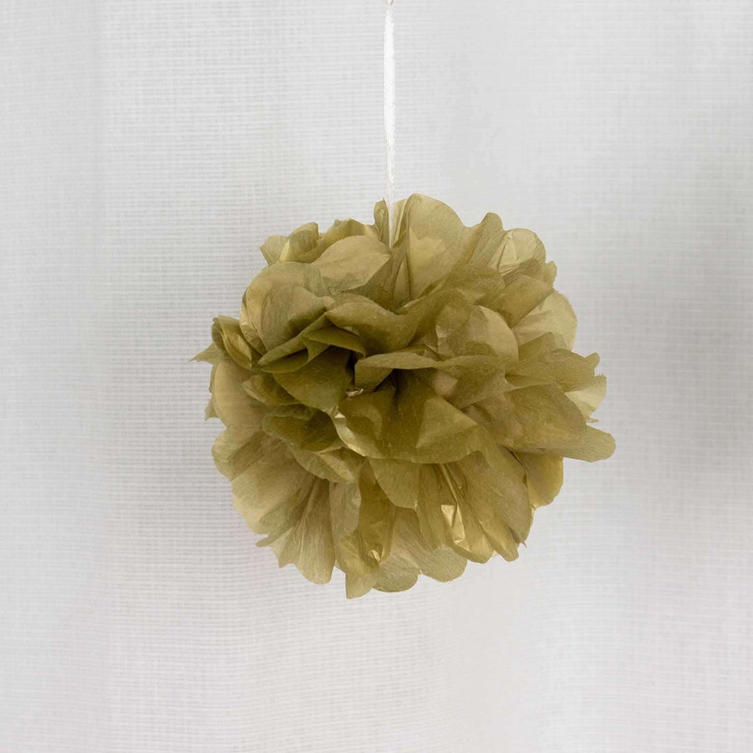 Gold tissue paper pom pom decoration hanging on a white background.