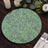 Green leaf-patterned round placemat on a wooden table with candles and flowers.