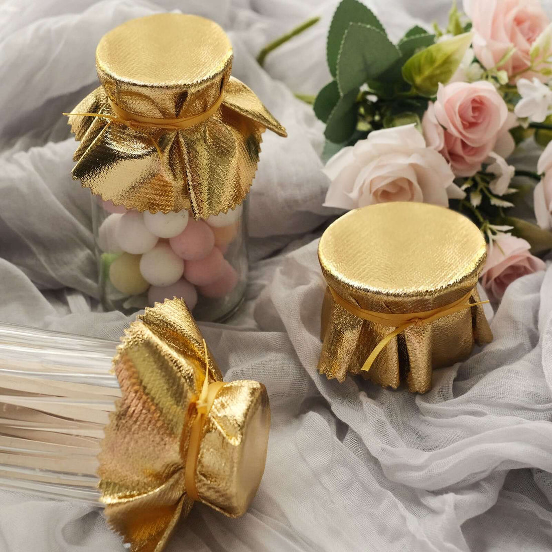 Gold-finished jar lids on decorative containers with pastel candy and flowers.