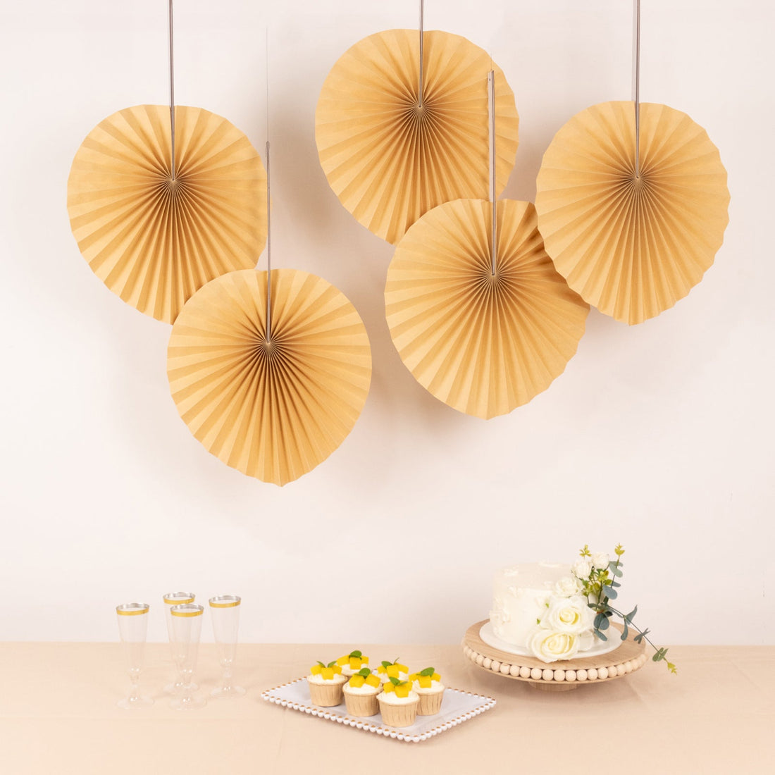Decorative paper fans with cupcakes and a cake on a table for a celebration.