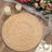 Woven natural fiber placemat on a rustic table with floral arrangement and candles.