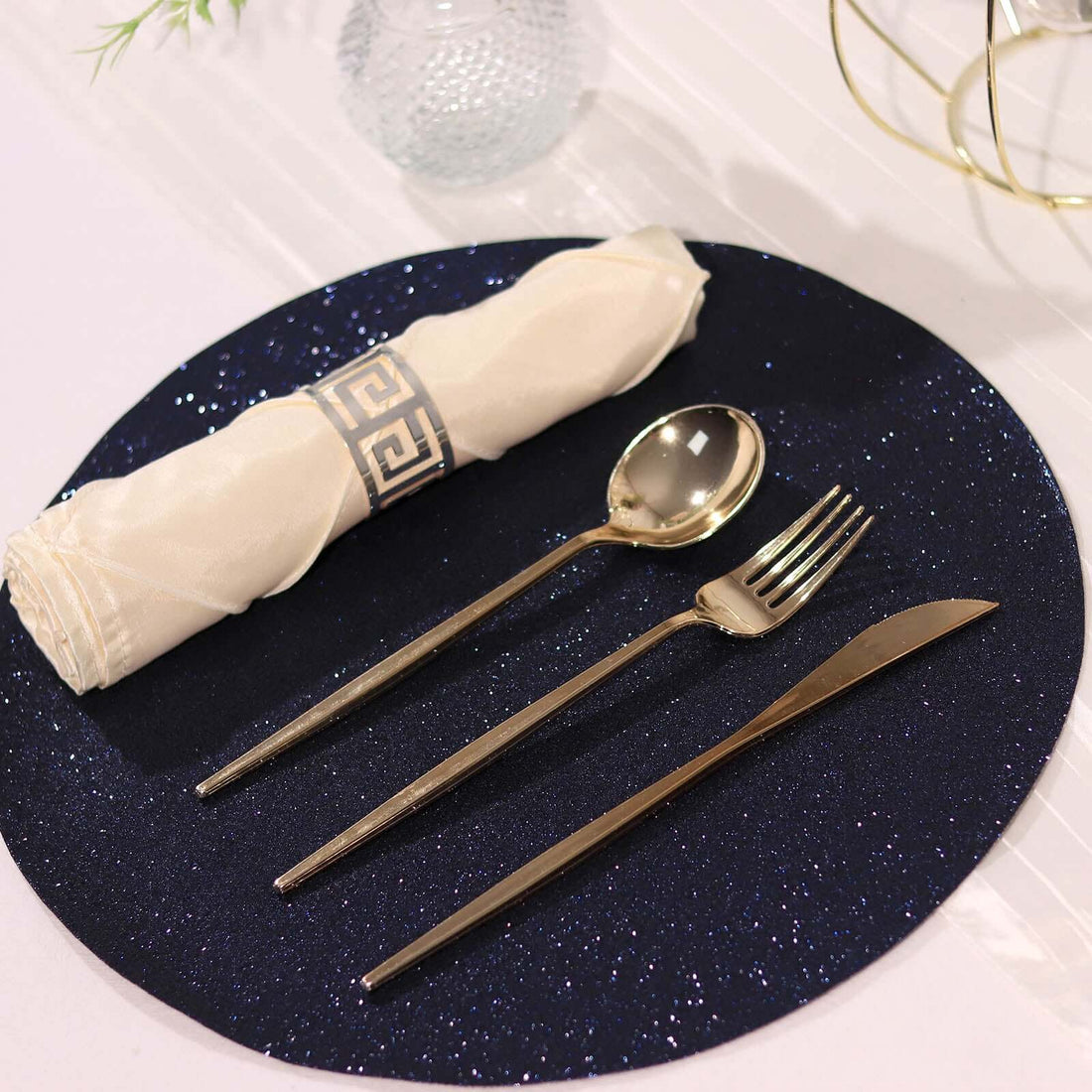 Elegant gold cutlery set on a navy glitter placemat with a rolled napkin.