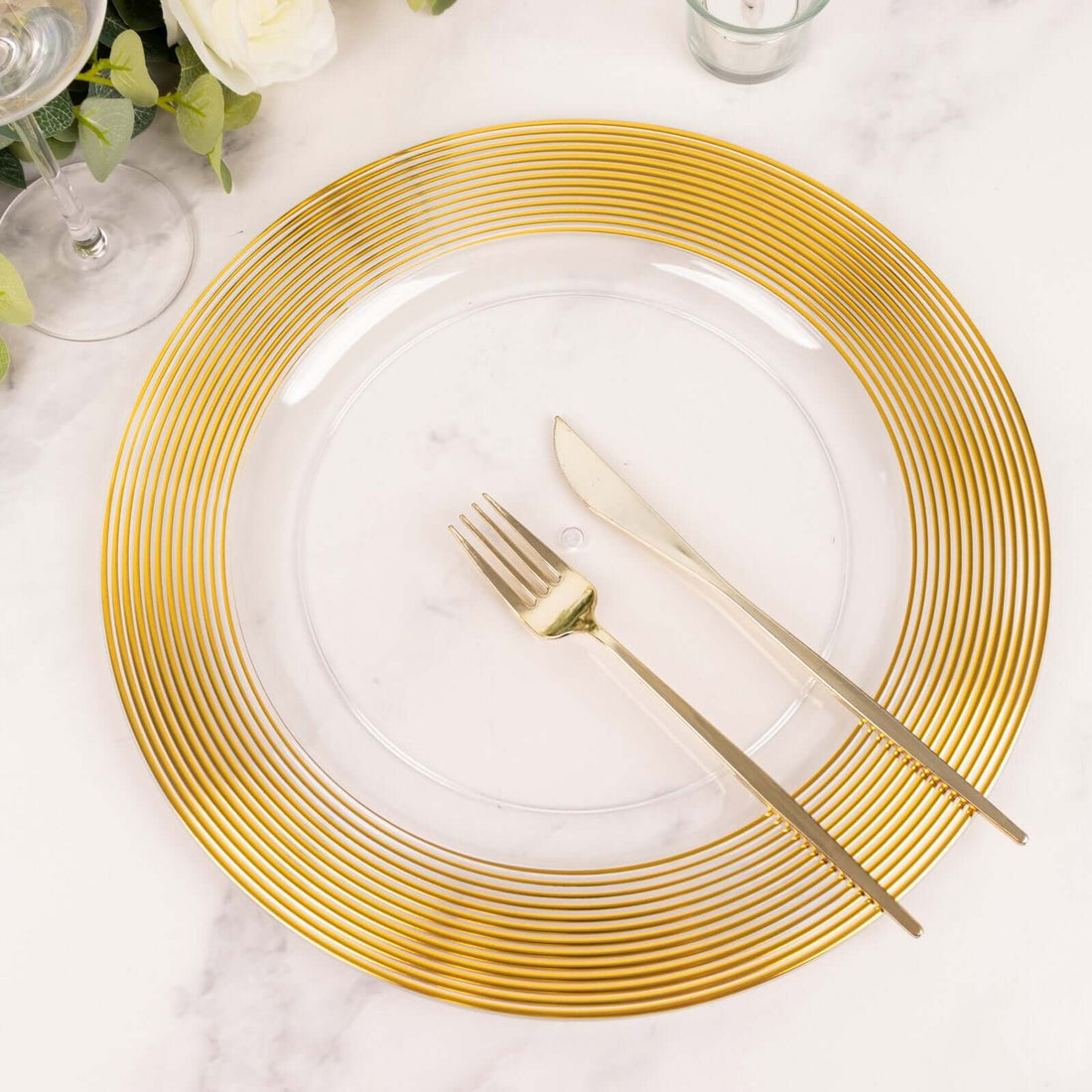 Gold-rimmed clear plate with cutlery on a marble surface.