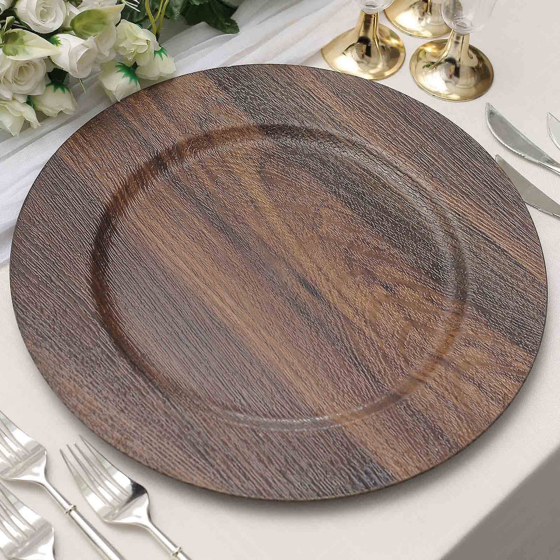 Wooden charger plate on a dining table setting with silverware and decor.