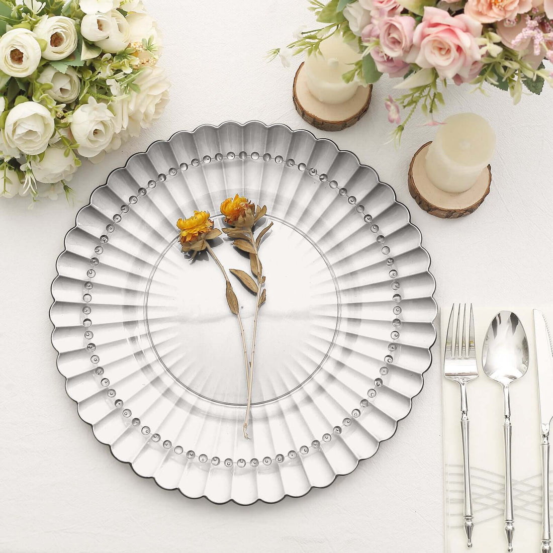 Elegant silver charger plate with dried flowers, set on a table with candles and flowers.