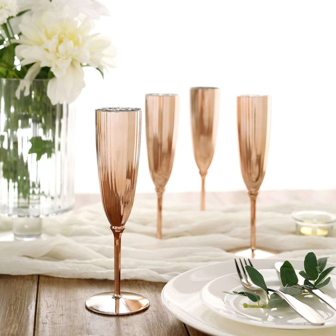 Rose gold champagne flutes set on a table with floral arrangement