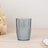 Blue decorative glass tumbler with textured design on a light wooden surface.