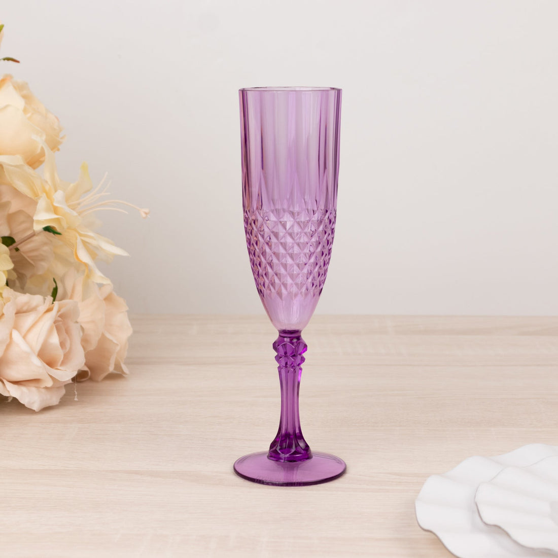 Purple champagne flute on a light wooden surface with floral accents.