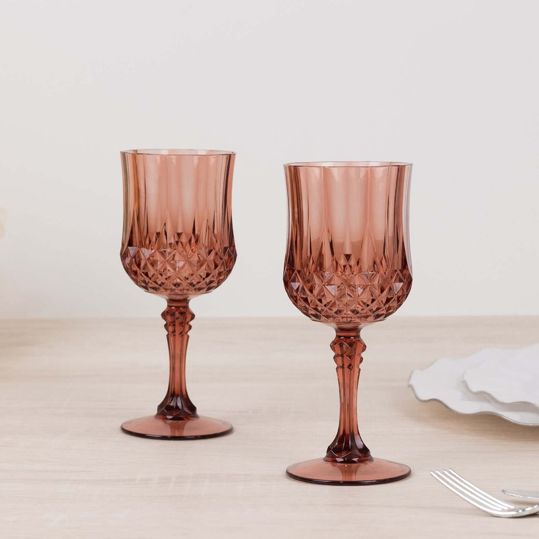 Set of two elegant rose glass goblets on a light wooden table.