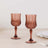 Set of two elegant rose glass goblets on a light wooden table.