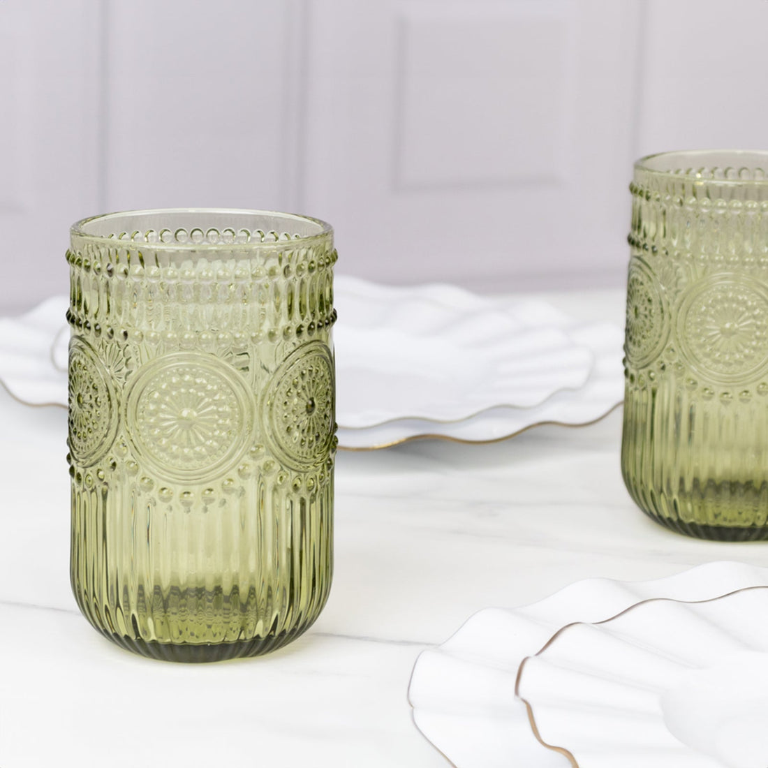 Textured green glass tumblers on a marble table with elegant white plates.