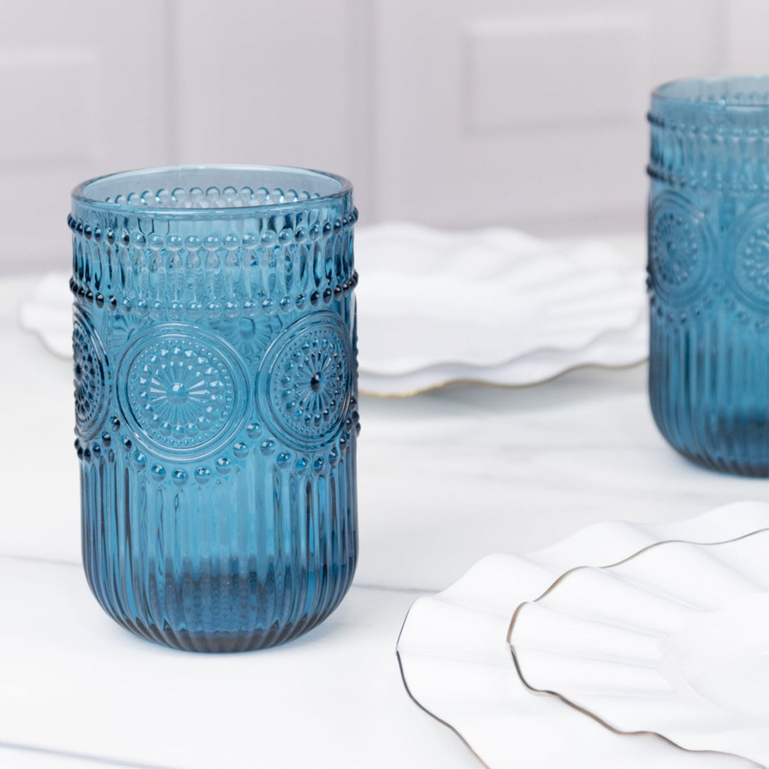 Blue vintage glass tumbler on a marble table with white plates.