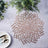 Decorative flower-shaped placemat on a grey surface with cutlery and greenery.