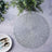 Textured round placemat on a dining table with greenery and cutlery.