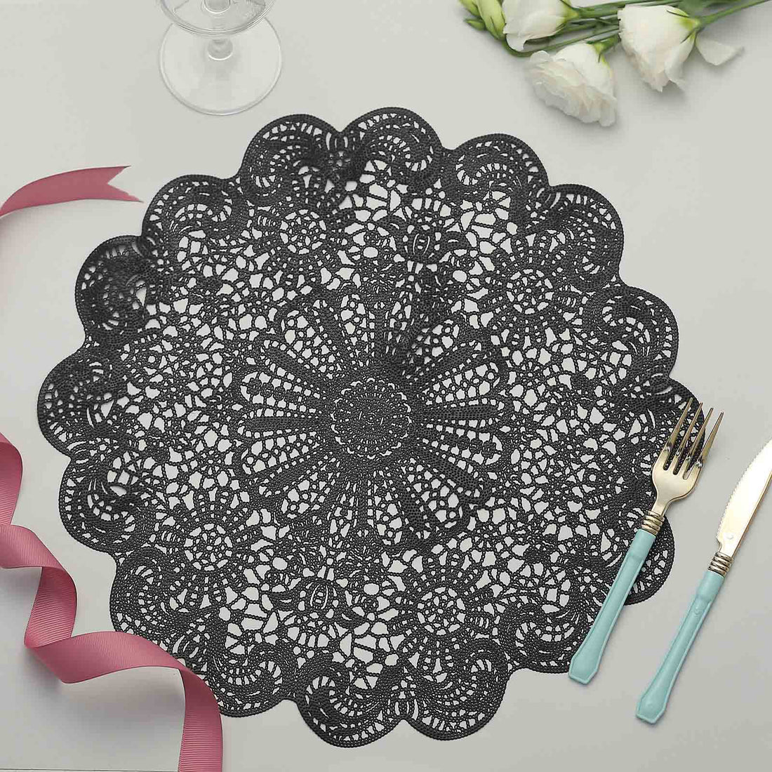 Black lace table mat with intricate floral design on a light surface.