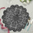 Black lace table mat with intricate floral design on a light surface.