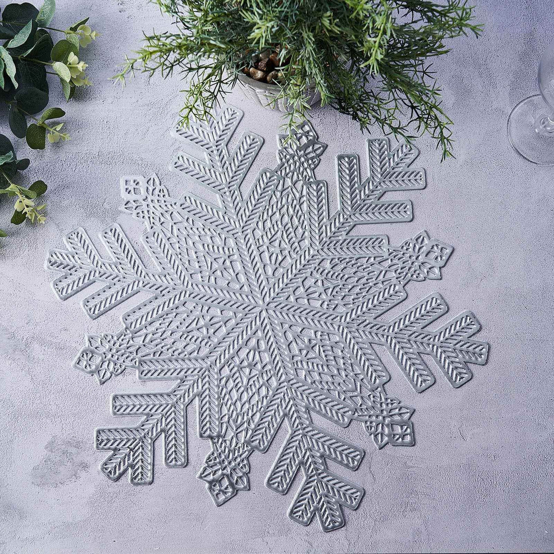 Gray snowflake placemat on a textured surface with greenery