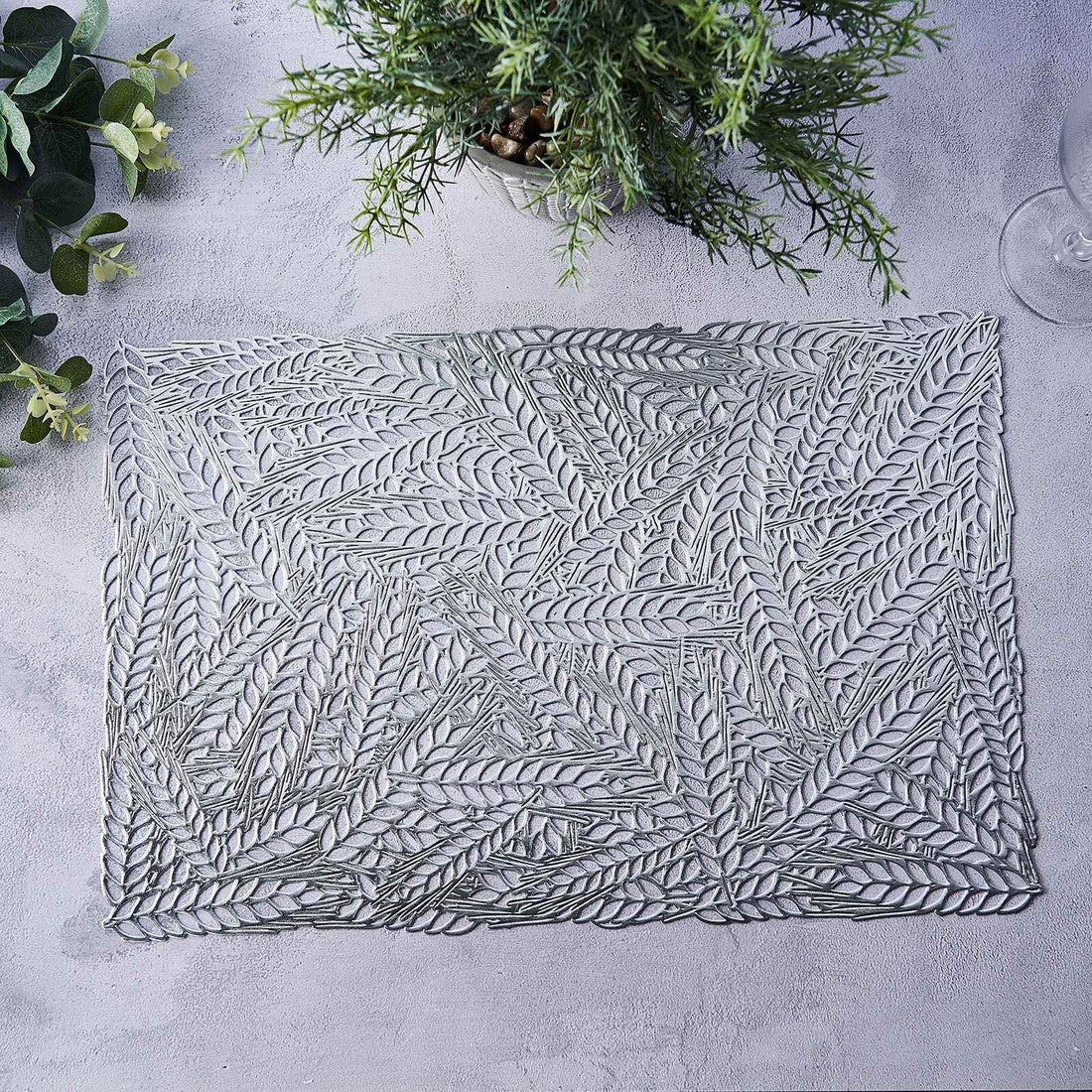 Decorative leaf-pattern placemat in gray on a textured surface.