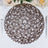 Brown woven placemat with intricate pattern on a dining table setting.