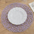 Purple woven placemat with a white plate on a wooden table.