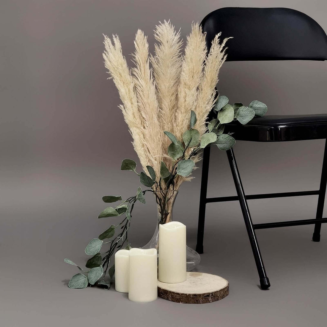 Pampas grass arrangement with candles and greenery beside a black chair.