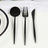Black cutlery set including spoon, fork, and knife on a white tablecloth.
