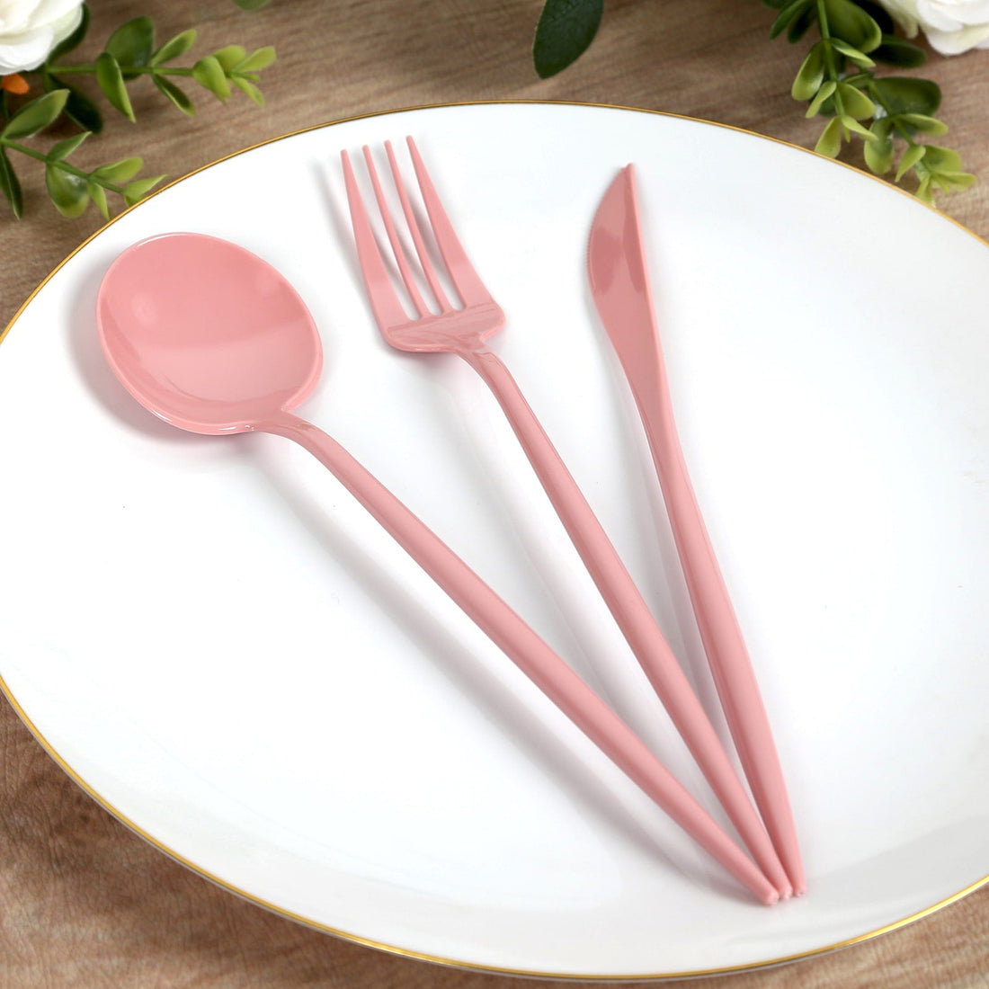 Pink plastic cutlery set on a white plate, including a spoon, fork, and knife.