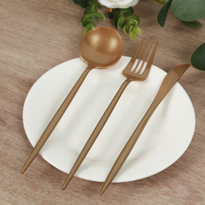 Gold stainless steel cutlery set on a white plate with a wooden background.