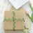 Gift box wrapped in green vines on a textured surface with flowers.
