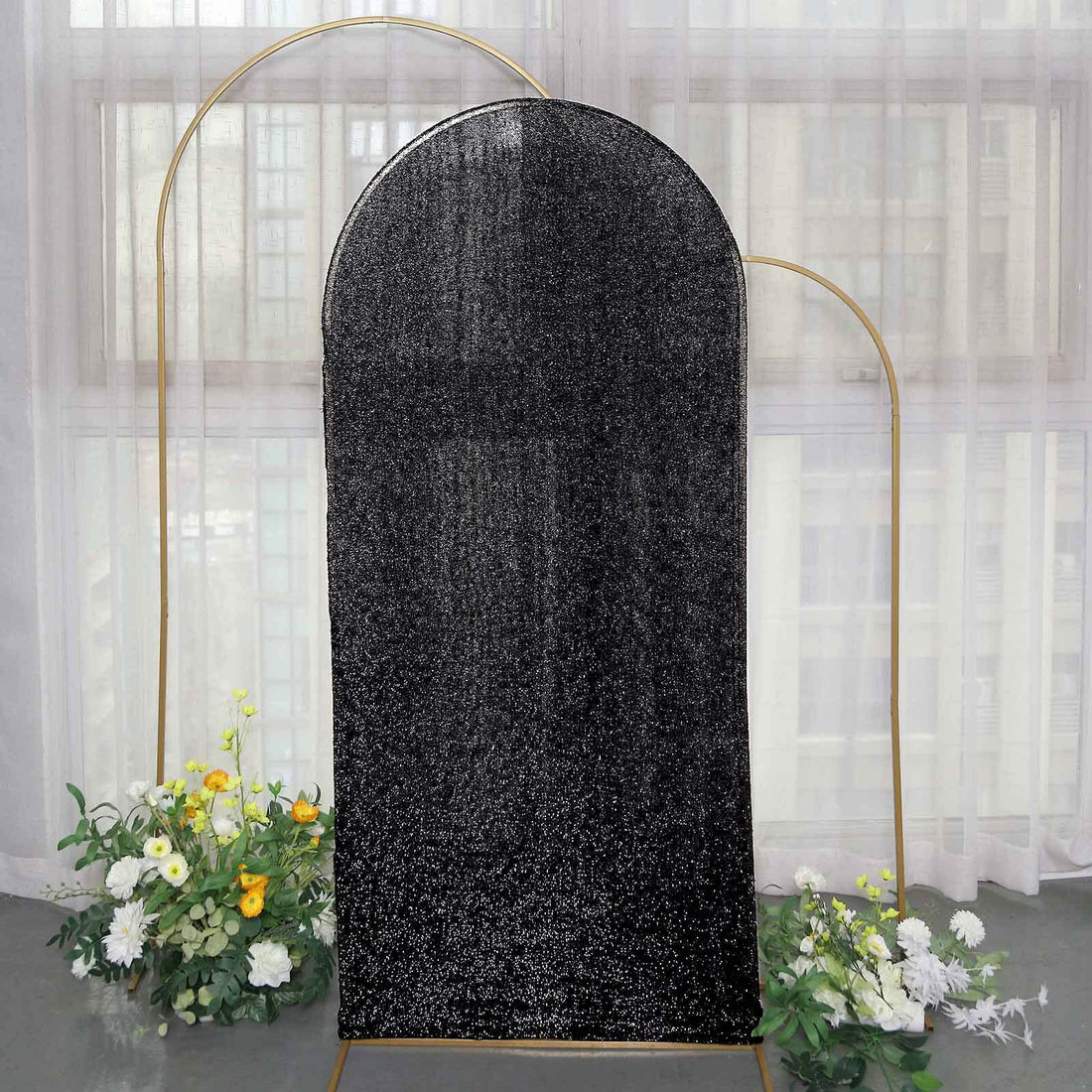Black glitter arch backdrop with floral arrangements in soft natural light.